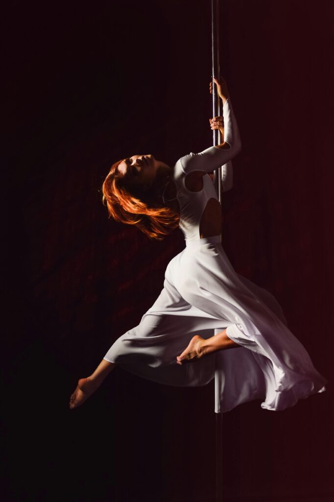 Graceful pole dancer in white dress showcasing strength and agility.